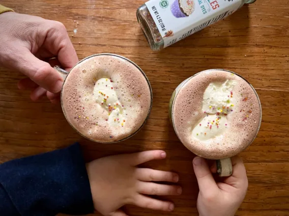 Two cups of hot chocolate are shown being picked up by adults and kids.