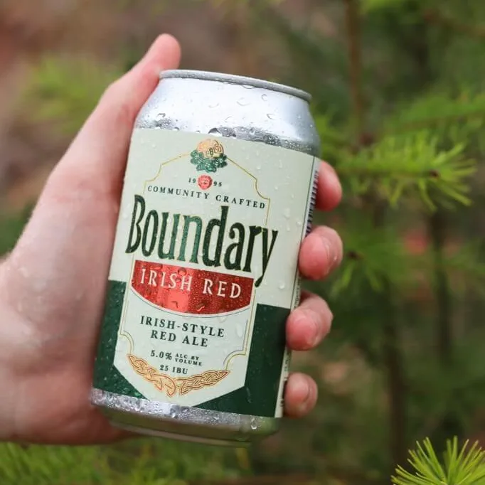 Someone holds a can of Irish Red Ale in the woods.