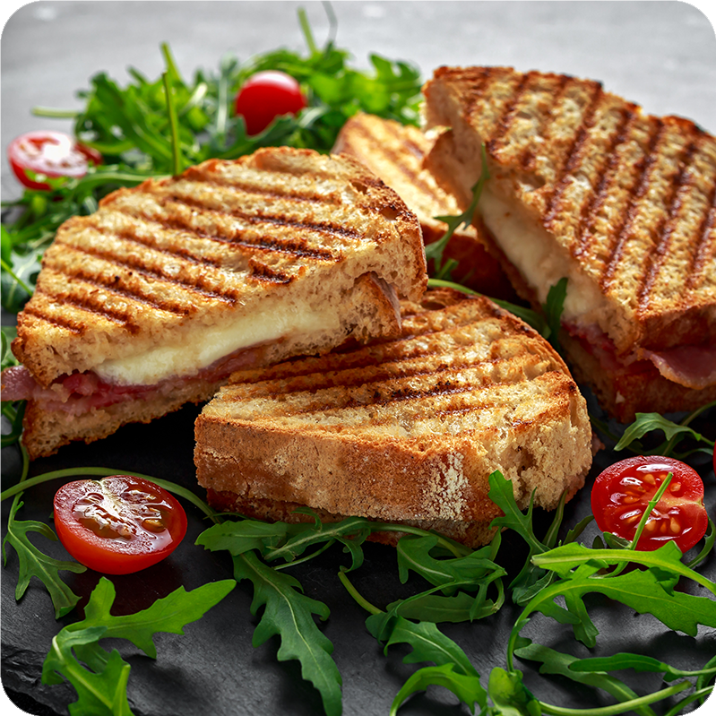 A grilled cheese sandwich with bacon on a bed of arugula and tomatoes, on top of a flat gray surface